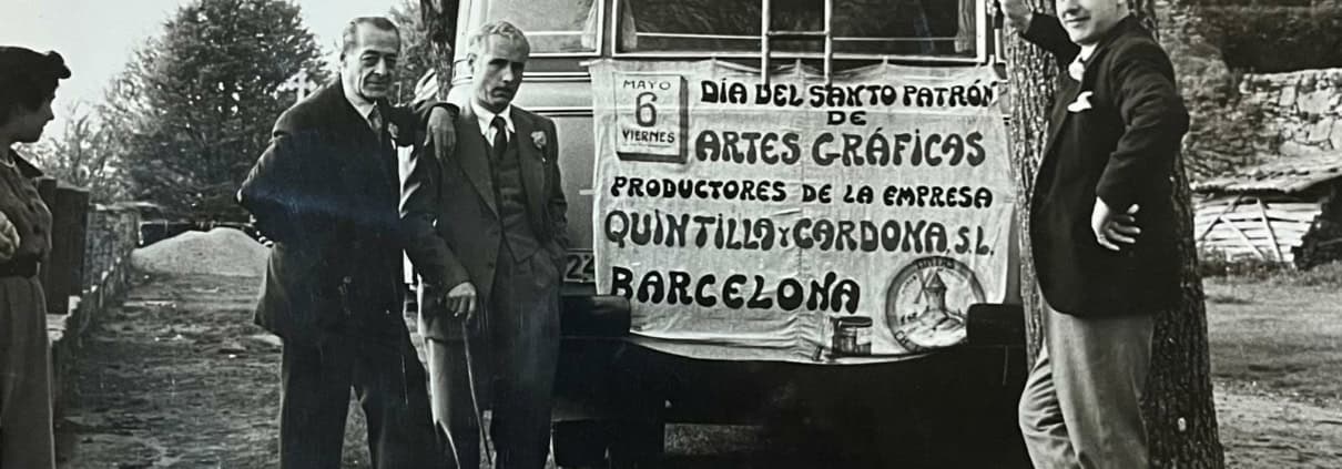 Trabajadores de la imprenta Quintilla y Cardona S.L. de Barcelona celebrando el Día del Santo Patrón de las Artes Gráficas el 6 de mayo, frente al autobús de la empresa con pancarta, años cincuenta